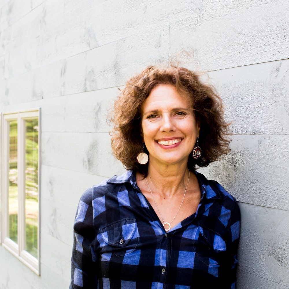 Kathy Engel in blue shirt smiling and leaning against a wall