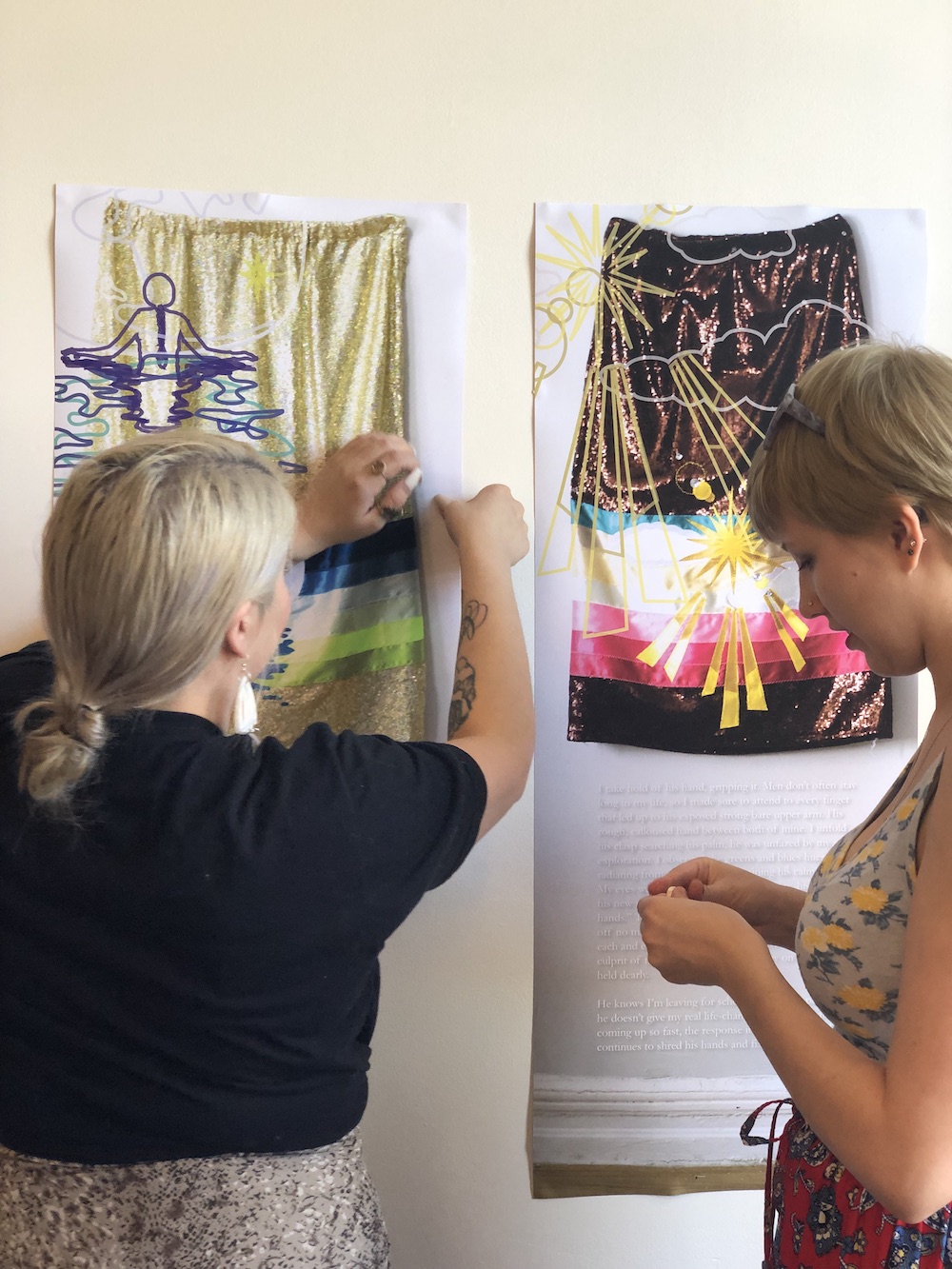 Two women hang tapestries on a wall