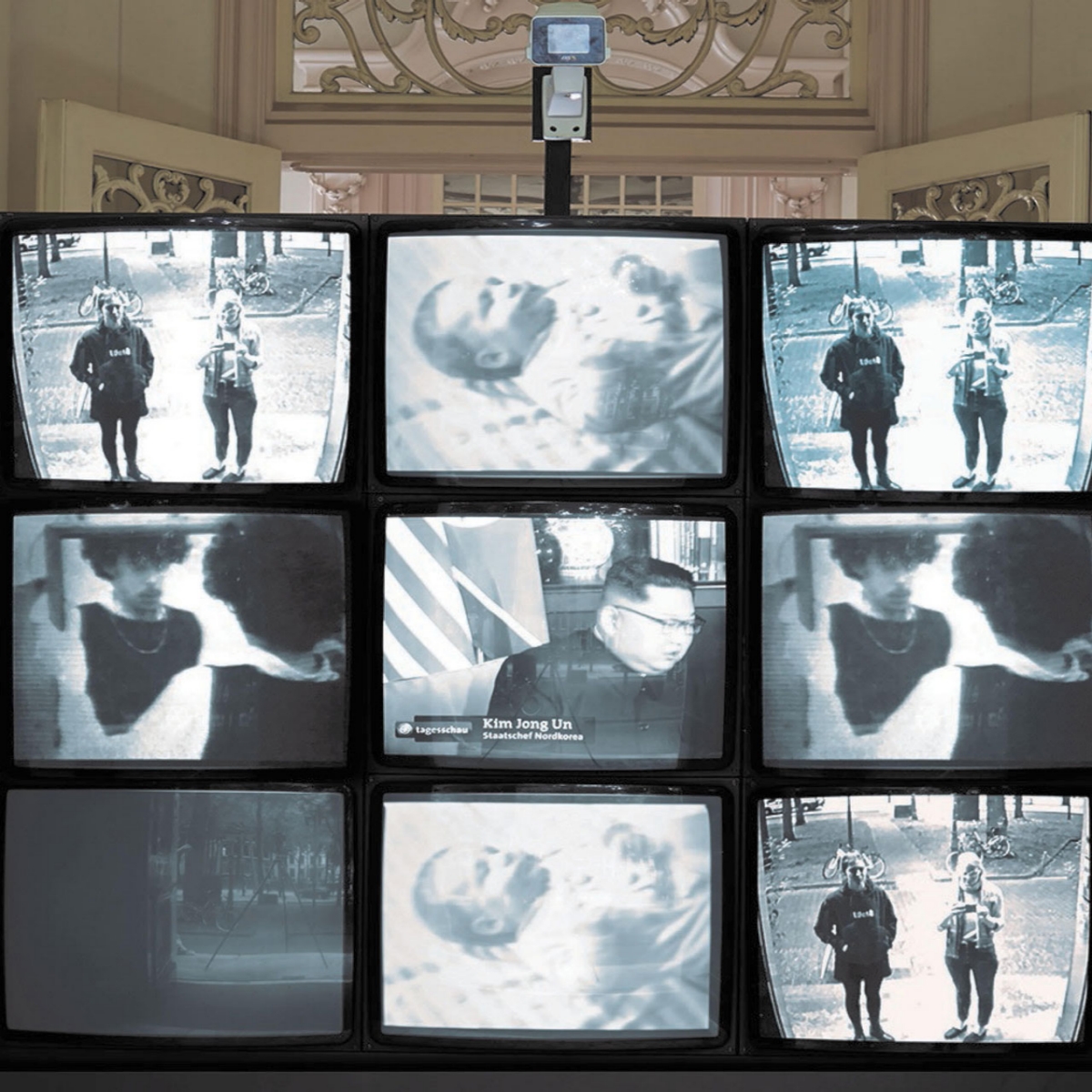 nine surveillance monitors in a grid, setup in front of open doors and a camera.