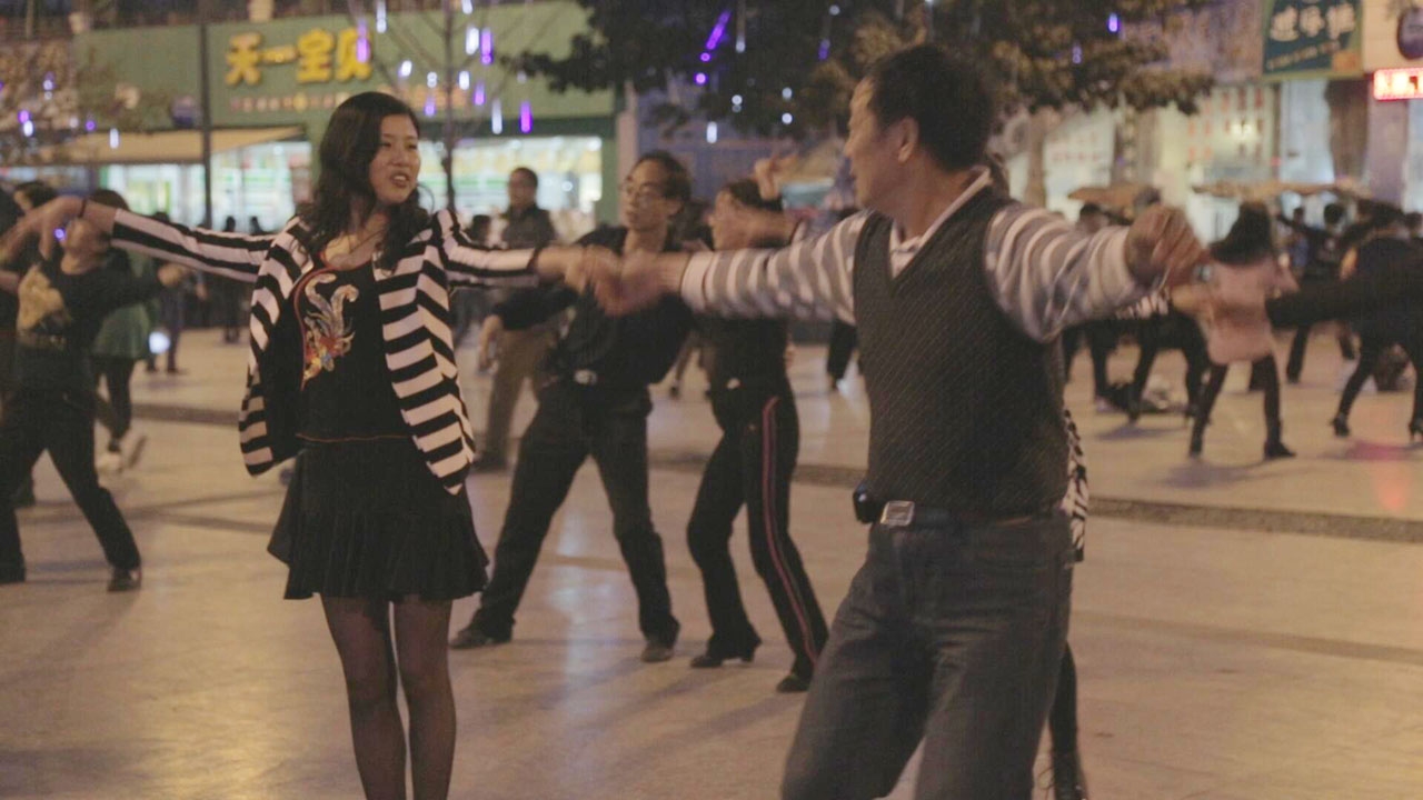 A couple dances in the street. Many dancers are visible in the background.