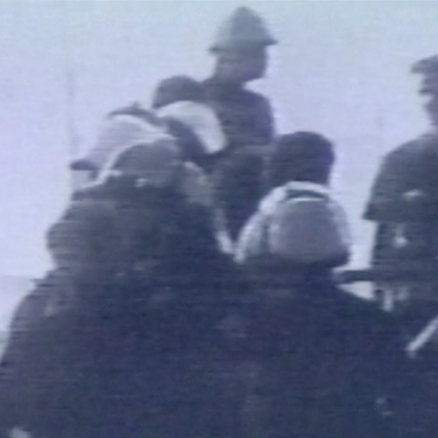 Grainy image of police in riot gear, standing in front of people wearing regular clothing. 
