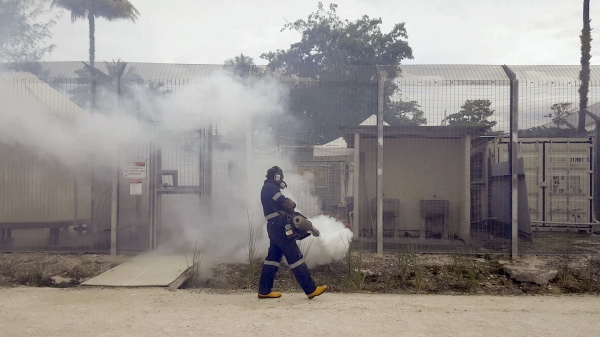 Person in a hazmat suit wearing a gas mask walking in front of a detention facility.