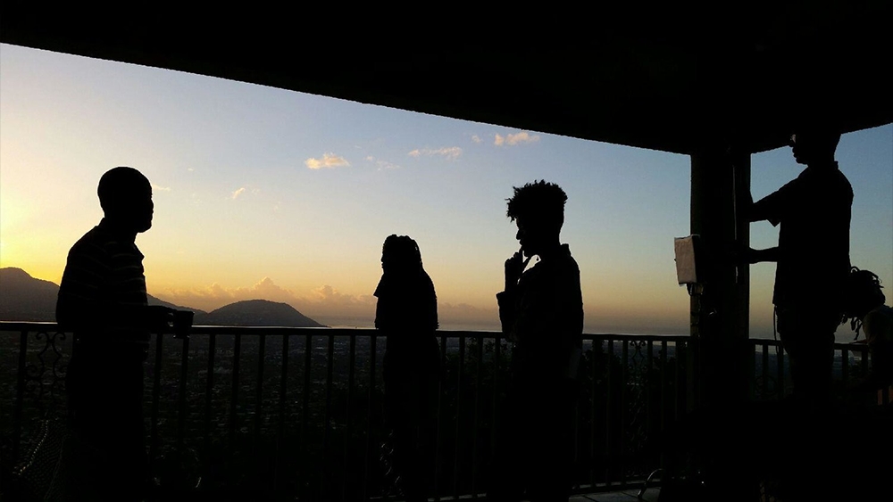 Film still from "Cross My Heart." Image of 4 people standing on a balcony with beautiful mountains and sky.