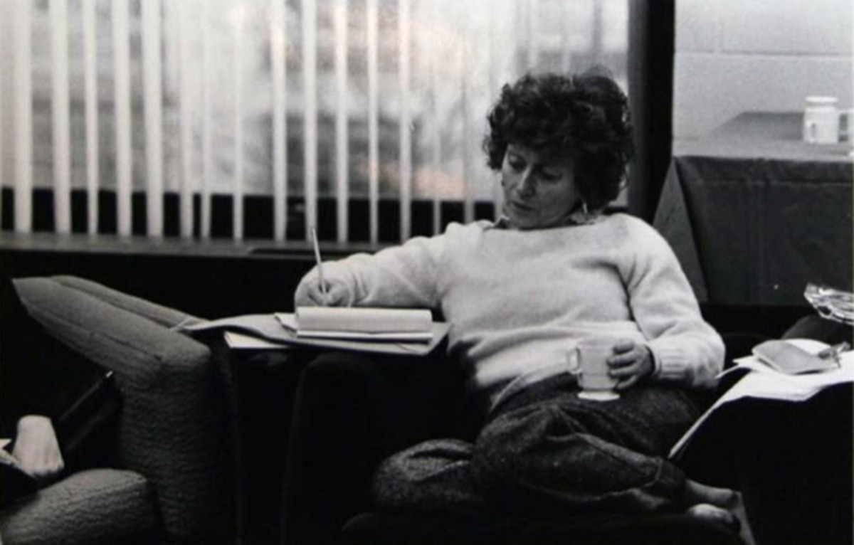 a younger Red Burns sitting on a couch with a mug writing on a notepad