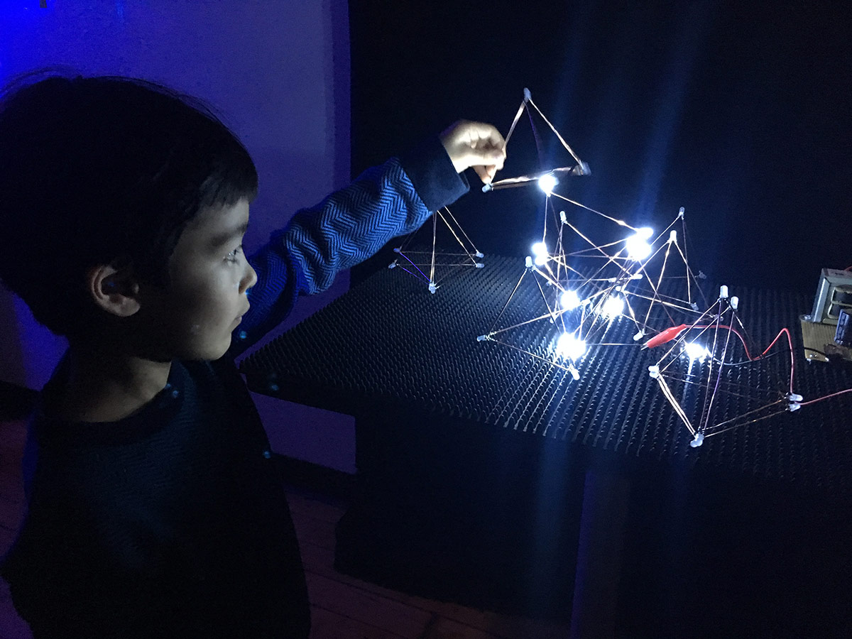 a boy playing with metal triangle shapes lit up by LED's
