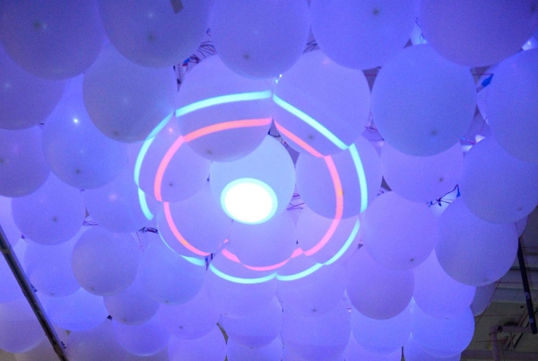 Dozens of balloons on the ceiling with a projector illuminating purple and a circle.