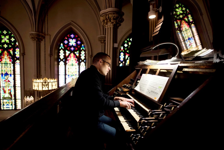 a man playing an organ with stained glass in the background