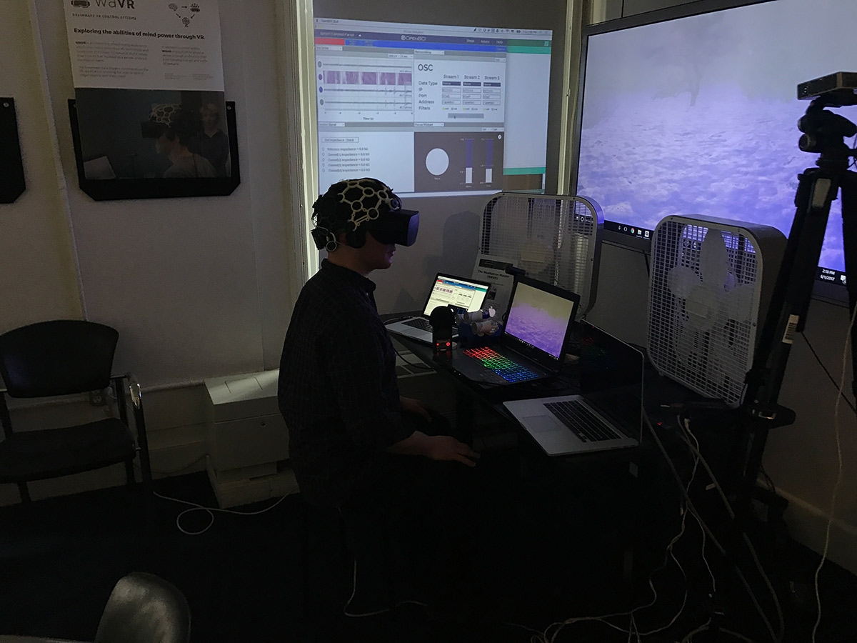 A person sitting in a dark room wearing a brainwave helmet and VR headset