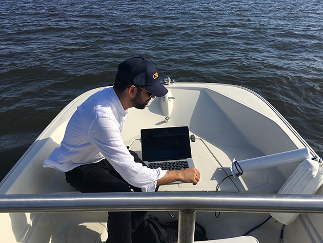 a man with a laptop sitting on the back of a boat in the water