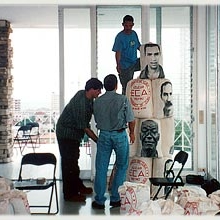 3 men setting up an installation of blocks with images of people's faces