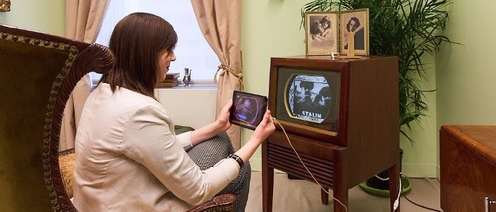A woman holding an Ipad in front of an antique TV set made of wood