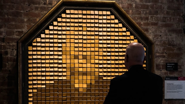 Man stands in front of wooden mirror at ITP which reflects back his face