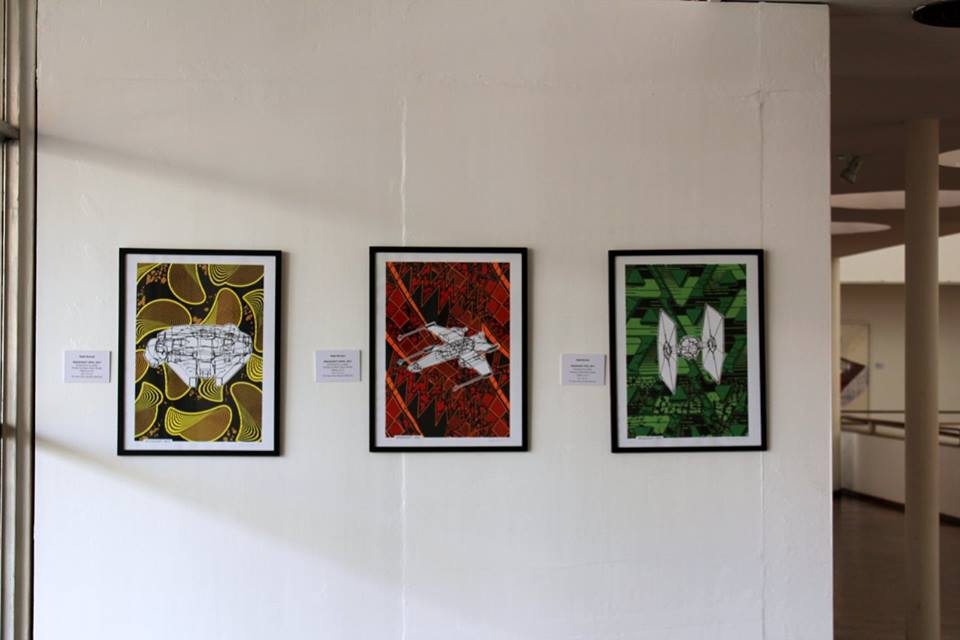 A gallery exhibit of three paintings displayed on a wall