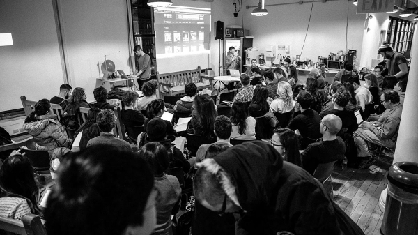 Black and white image of ITP students in the lounge listening to a lecture