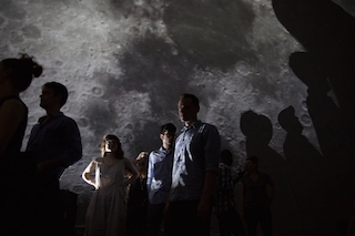 3 people with their shadows projected against a closeup of the moon in the background