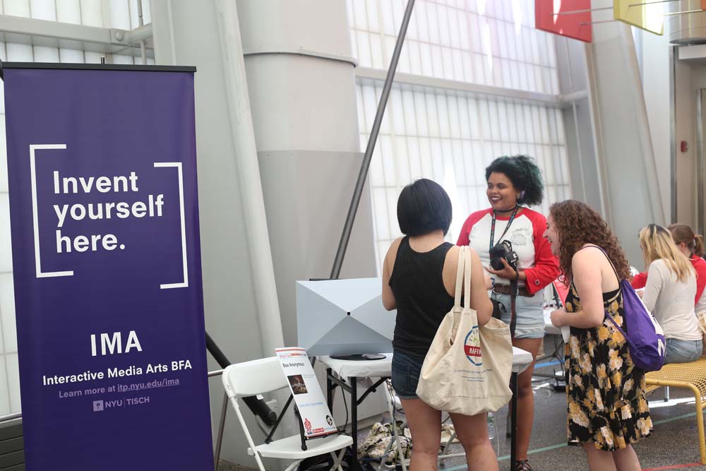A woman talking to 2 people with the IMA banner in the foreground