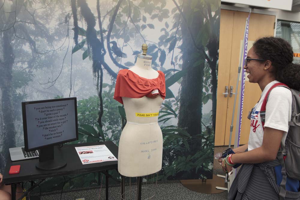 A person smiling as they look at a mannequin with a blouse and fake chattering teeth appearing from under the shirt