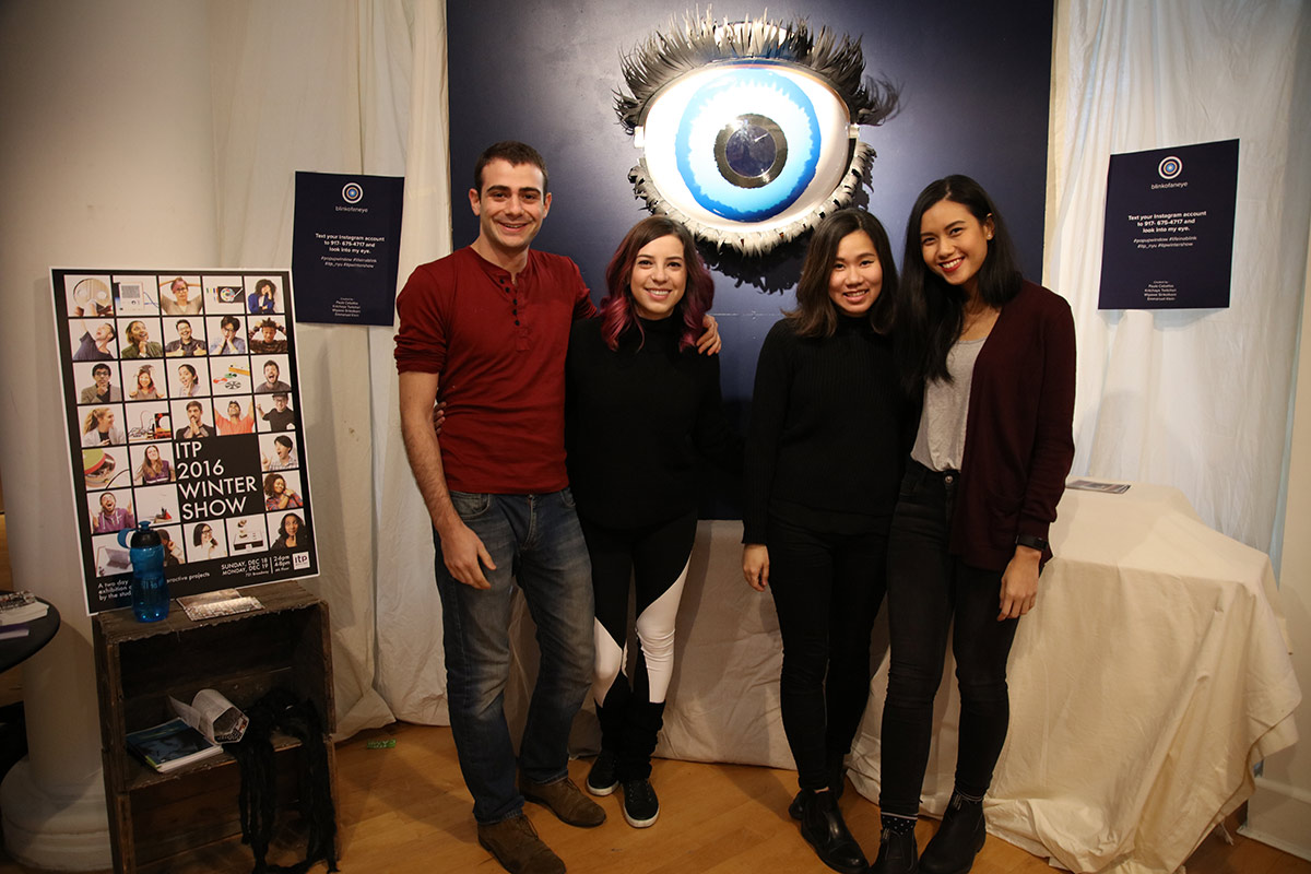 4 students smiling with a gigantic eye sculpture behind them