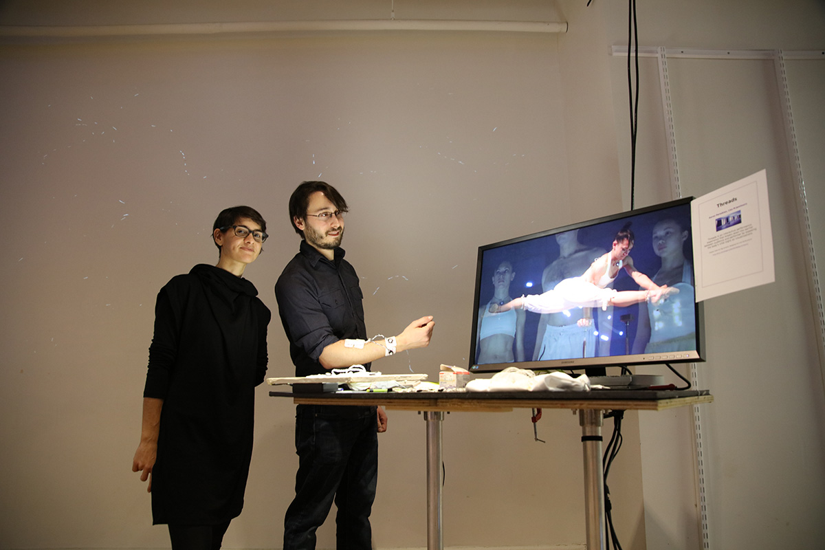Two people standing next to a monitor showing a dancer doing the splits