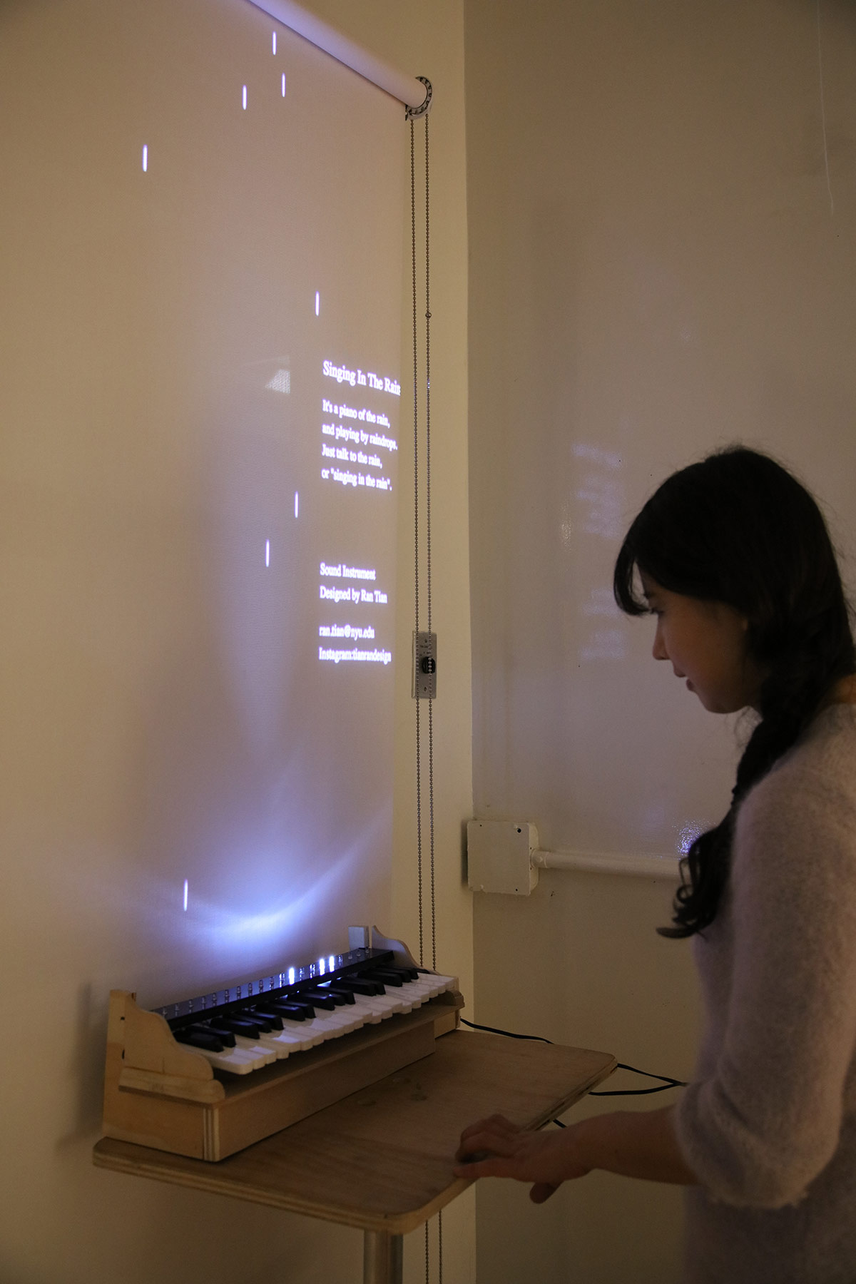a woman standing in front of a small keyboard that is triggering lights on the projection behind it