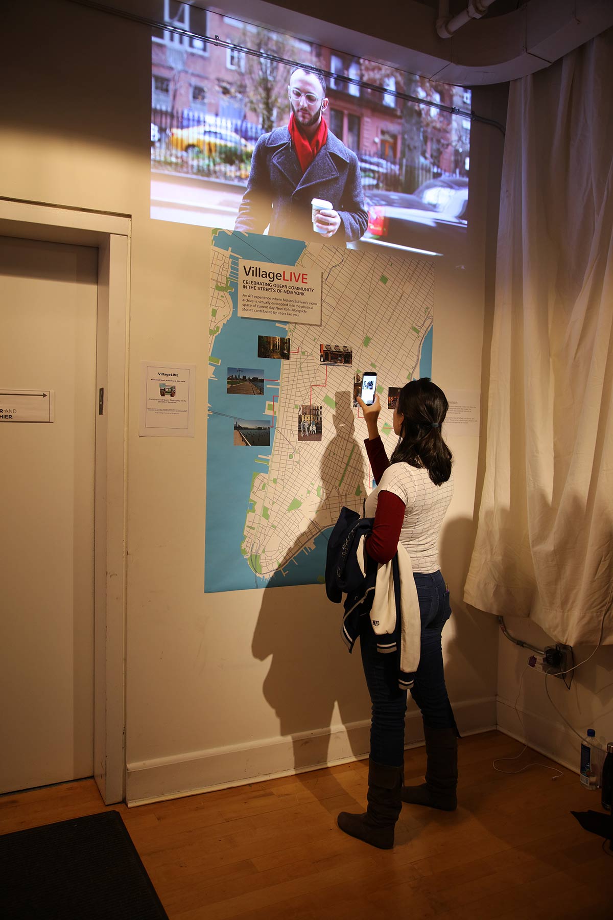 A person with an iphone in front of a map of lower Manhattan, that triggers video footage up above