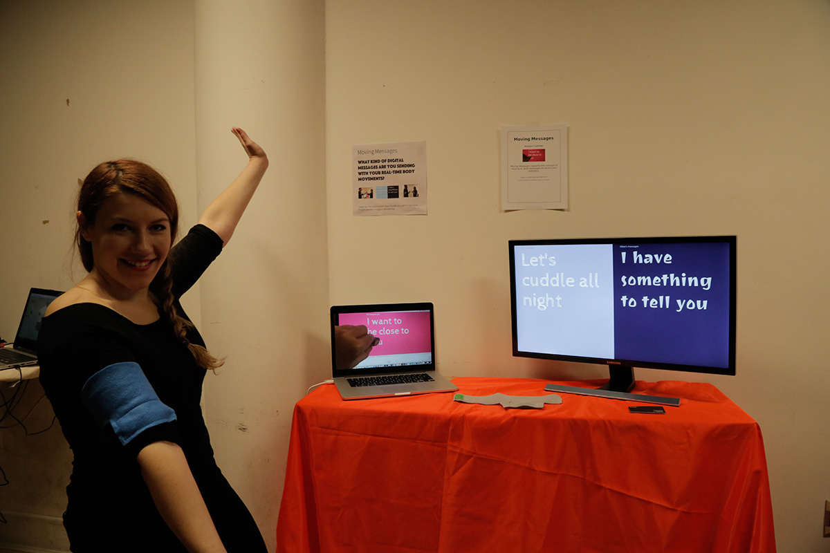A woman with her arms out, standing next to 2 monitors