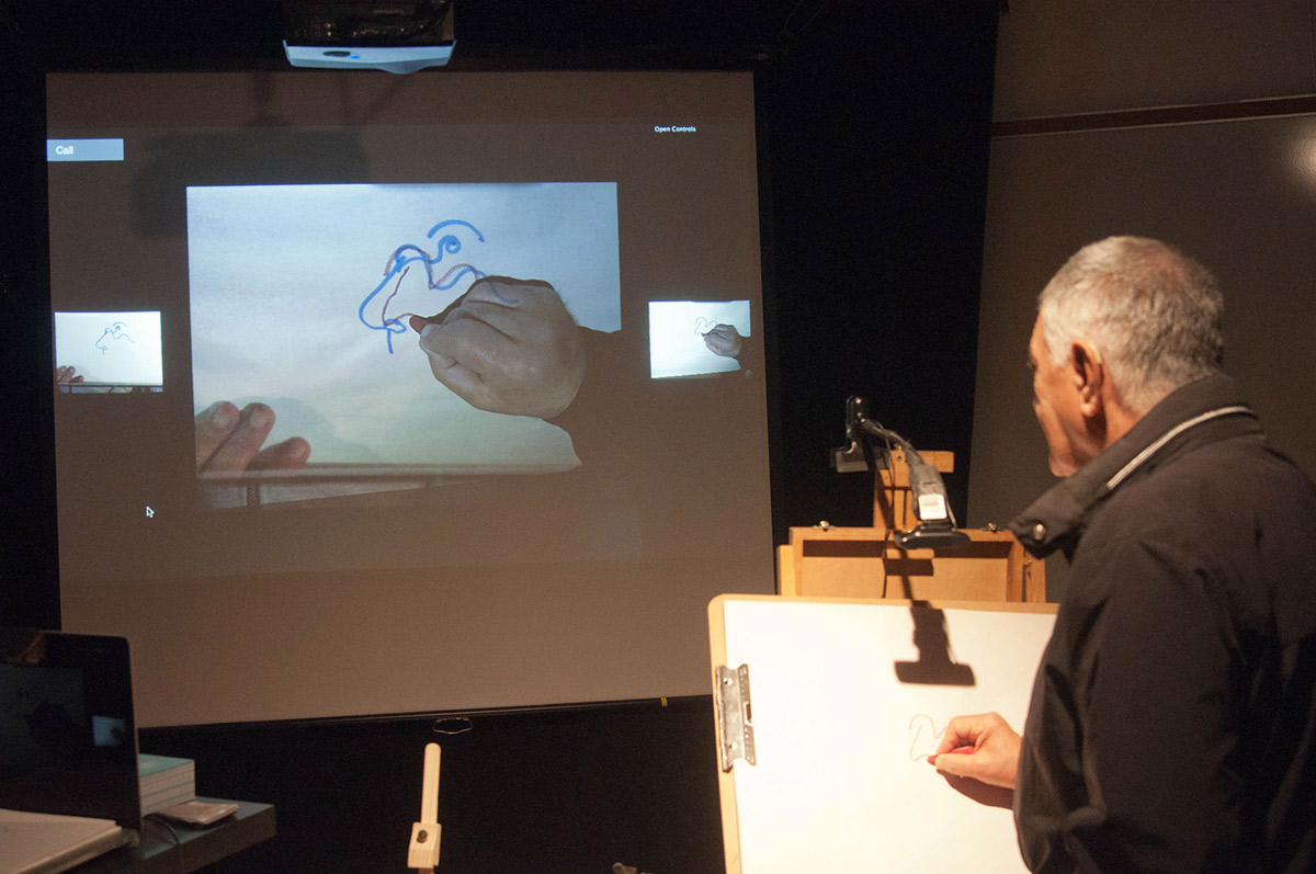 a man drawing on a pad which is projected on a screen with added AR visuals