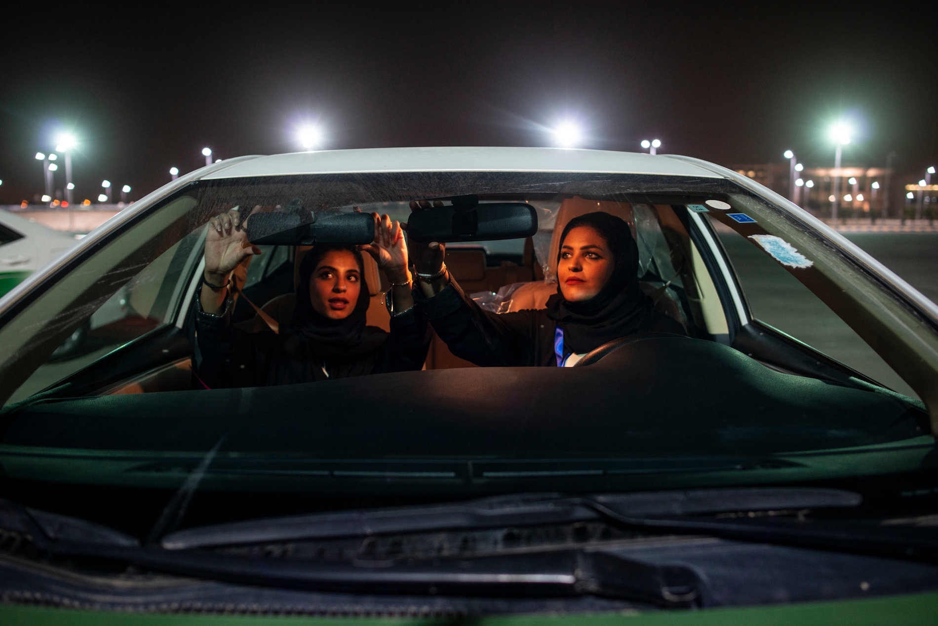 Photo through the front windshield of a car as two Saudi women adjust the mirrors