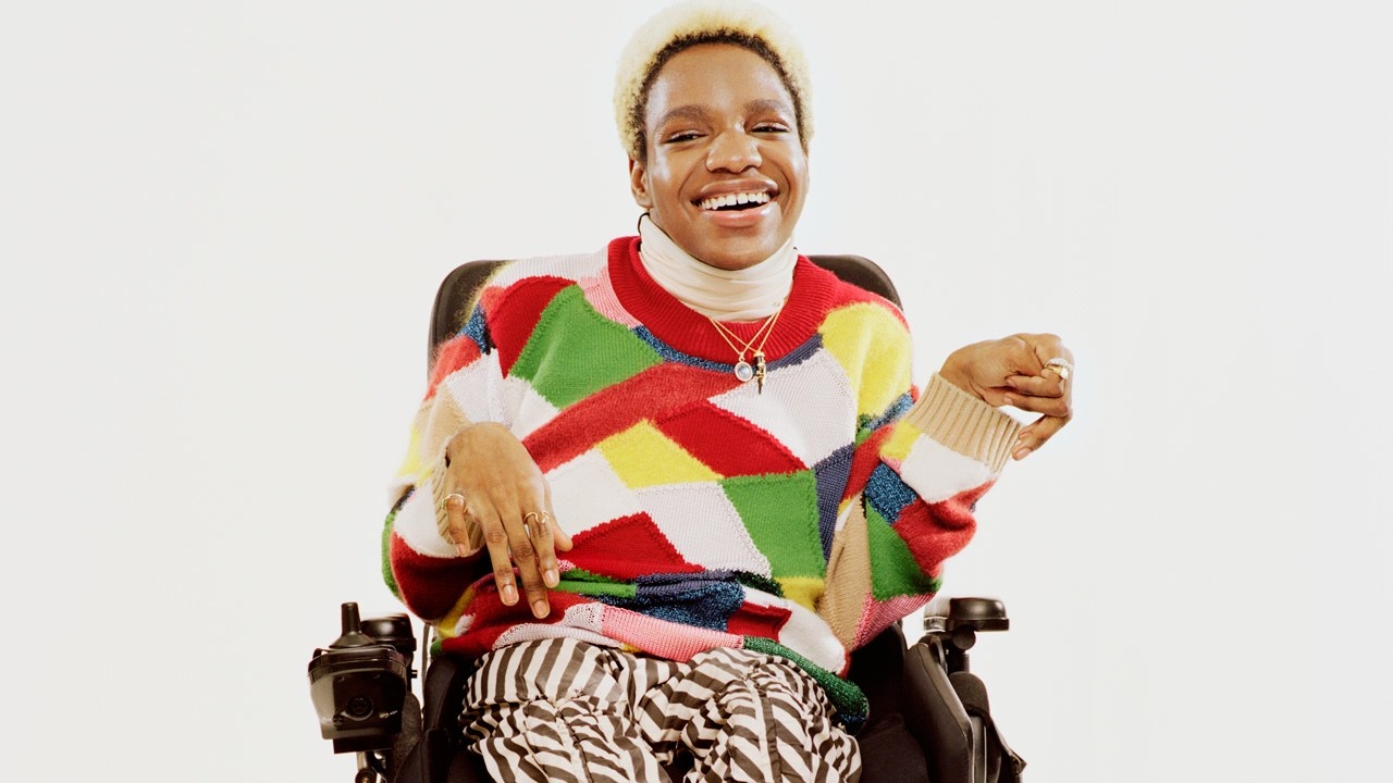 Disabled trans model Aaron Philips smiling in a colorful sweater