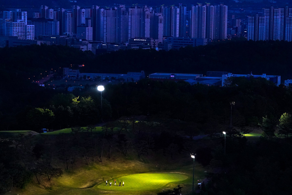 exterior photo landscape depicts spotlit golf course and cityscape in background