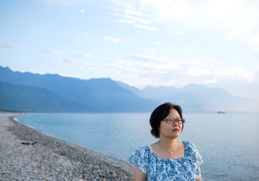 A woman stares into the distance with a dramatic seascape and mountains behind her