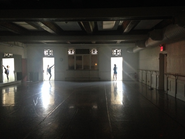 Three dancers backlit in the doorways of a dark dance studio.