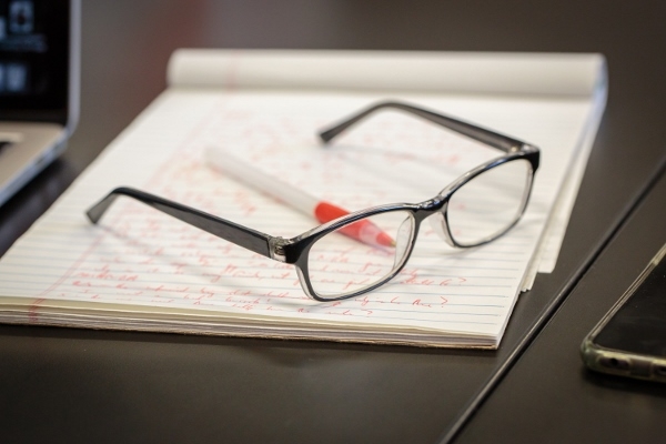 A pair of glasses set on top of a legal pad an red pen.