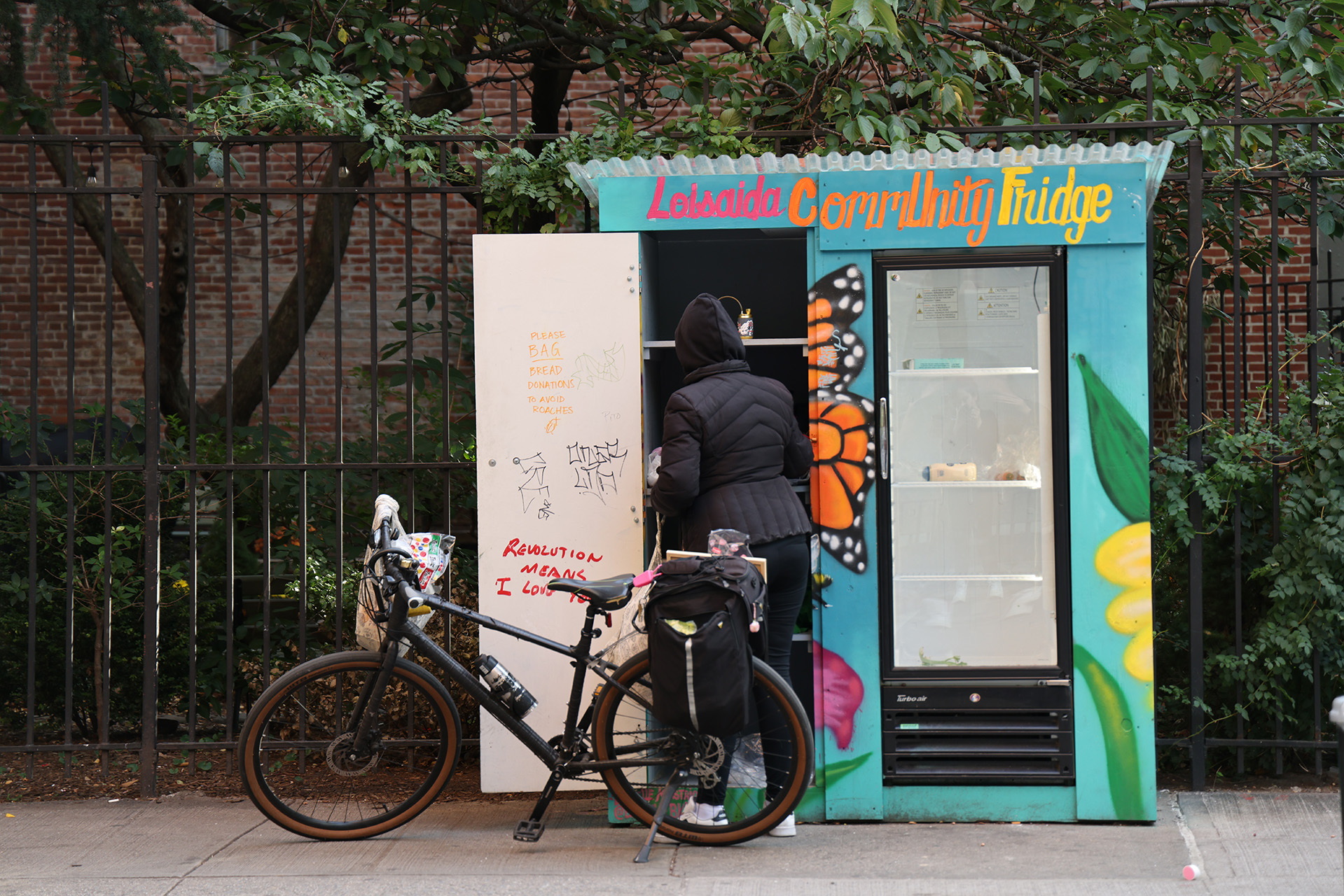 A student with a bike looks at a nearly empty community fridge
