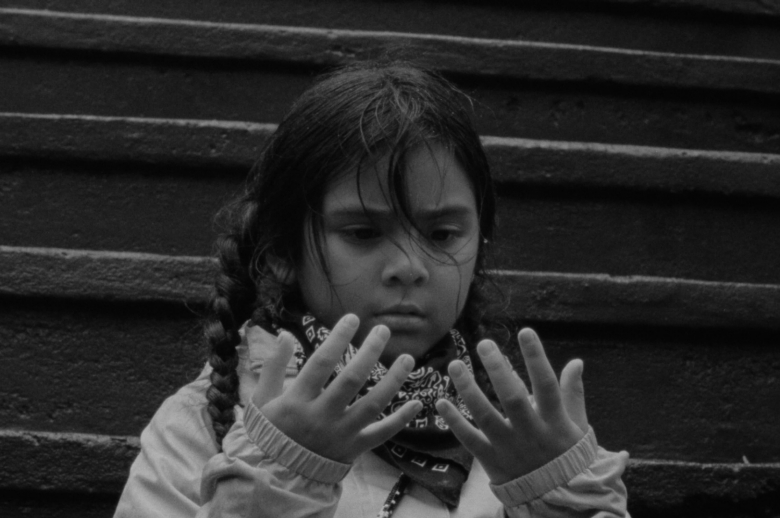 young Anishinaabe girl staring intensely at her outspread hands