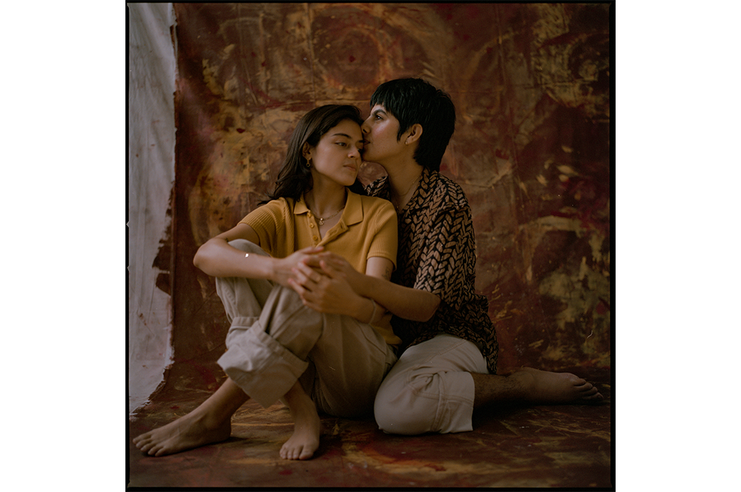 Two people sitting and hugging against a brown backdrop