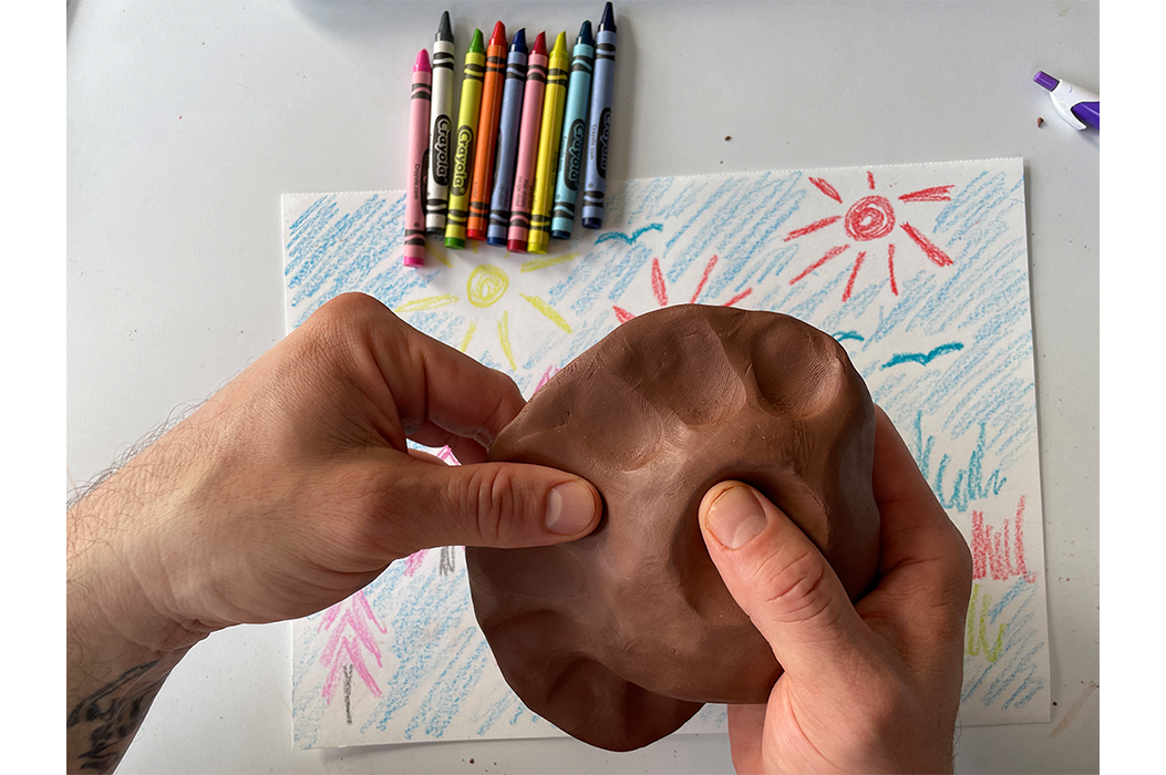Hand pressing into clay, crayons and drawing in the background