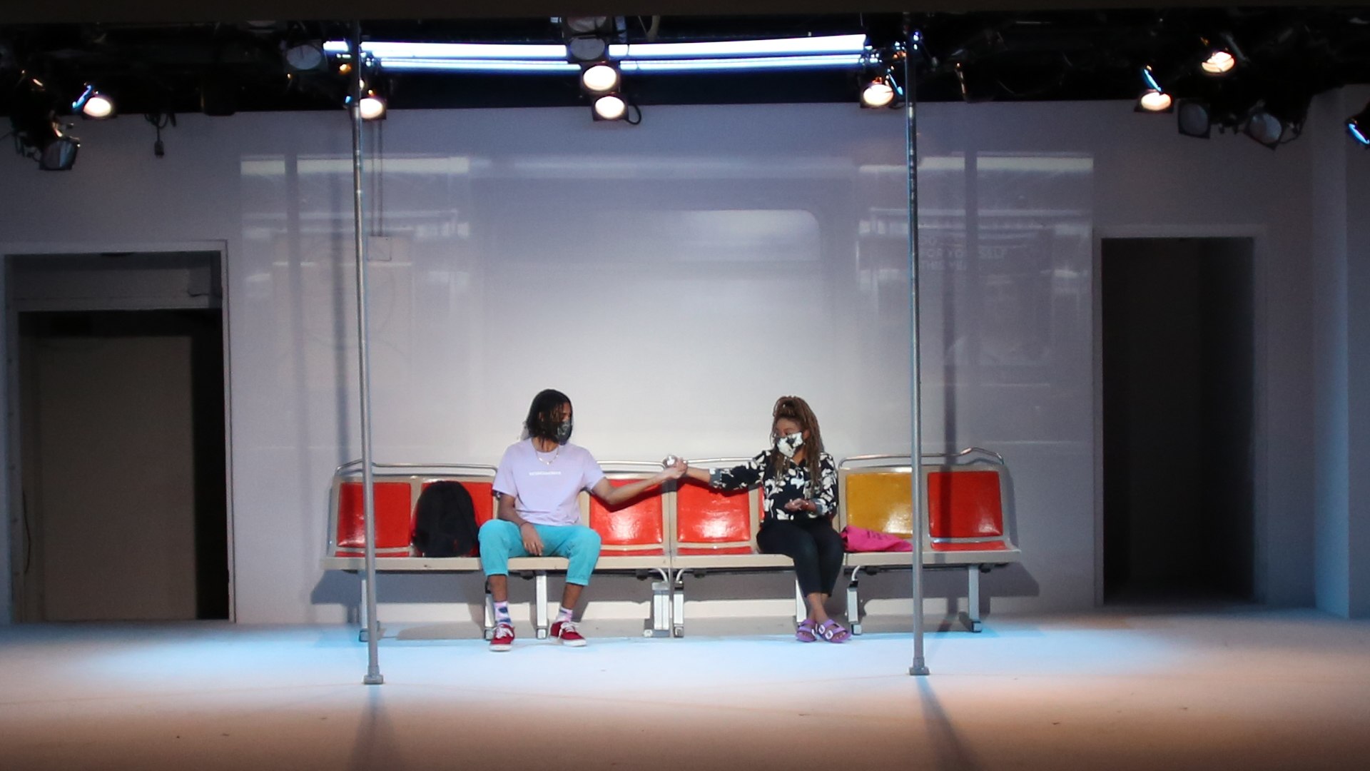 A theatre production set of two people giving a fist bump on a subway train