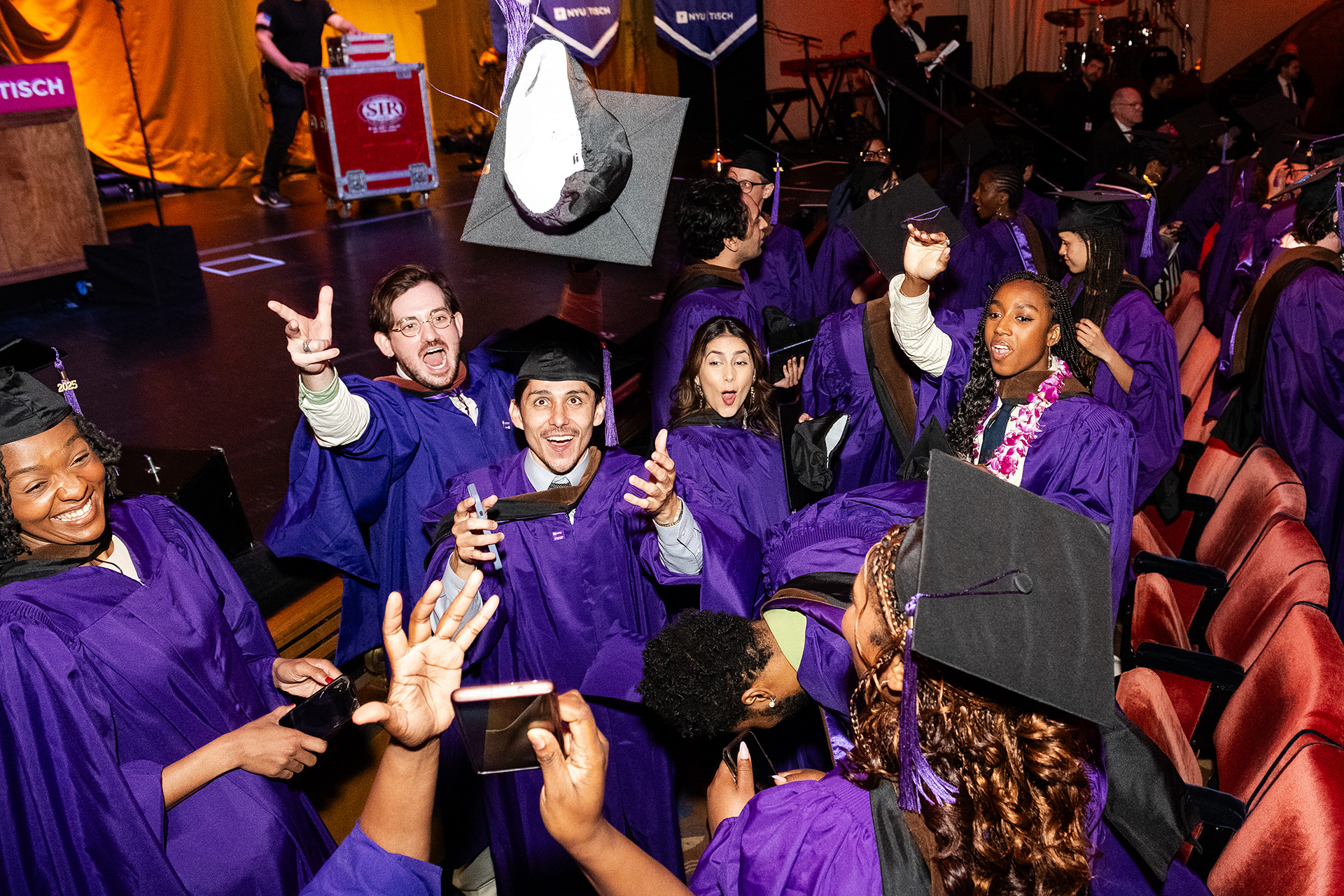 NYU Tisch graduates throwing their caps in the air