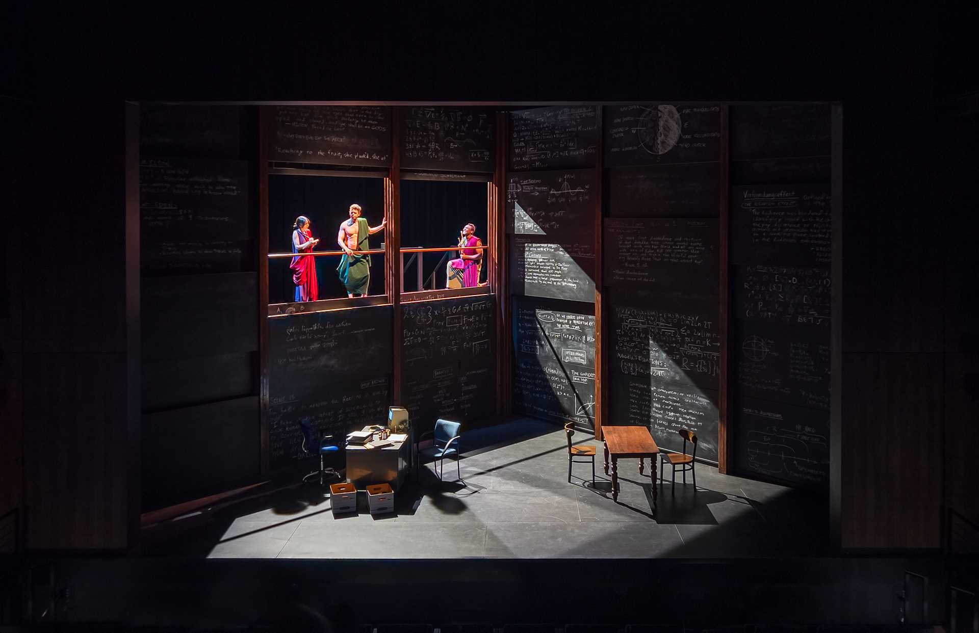 Students in a drama performance on a dark stage with brightly colored outfits