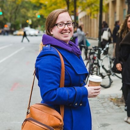 Jana Pickart weaubg blue coat and glasses, holding tan bag and coffee