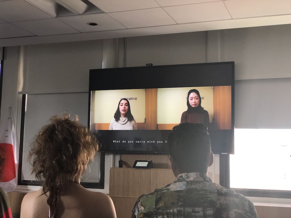 Photo taken from audience behind two people looking at a screen featuring two women side by side