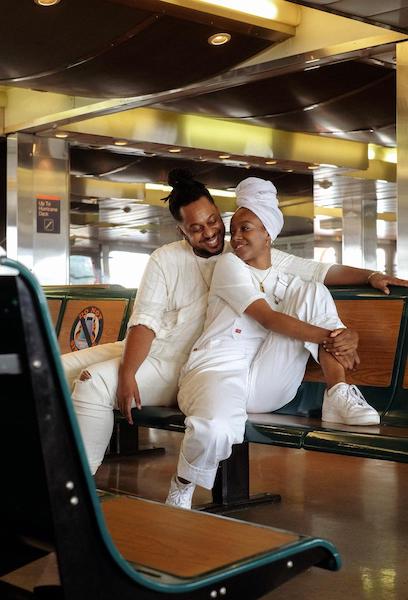 A picture of a Black couple wearing all-white while sitting on the Staten Island Ferry.