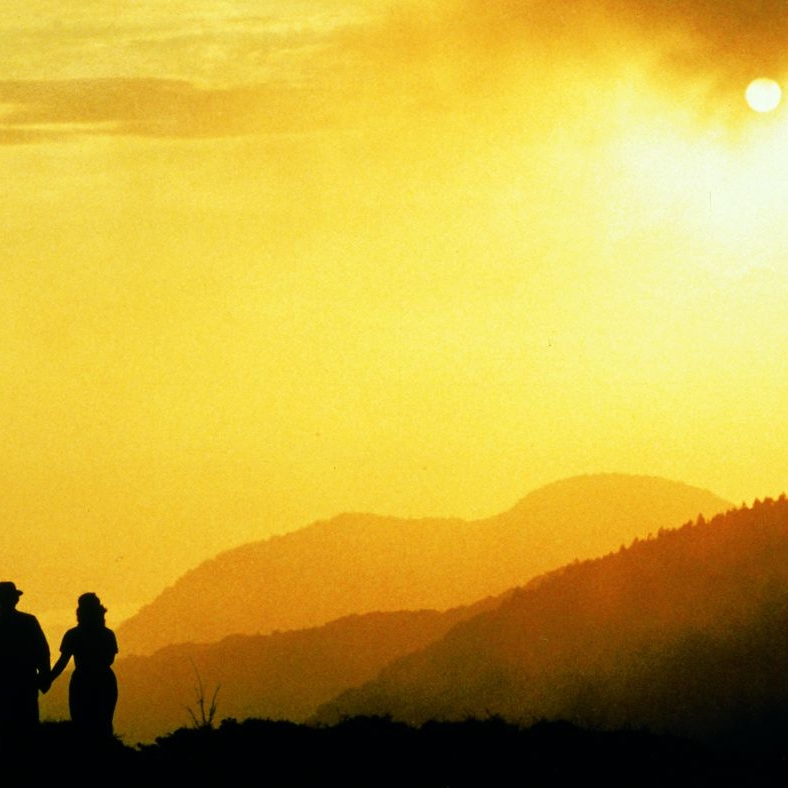 Three human figures silhouetted against a bright yellow sunset.