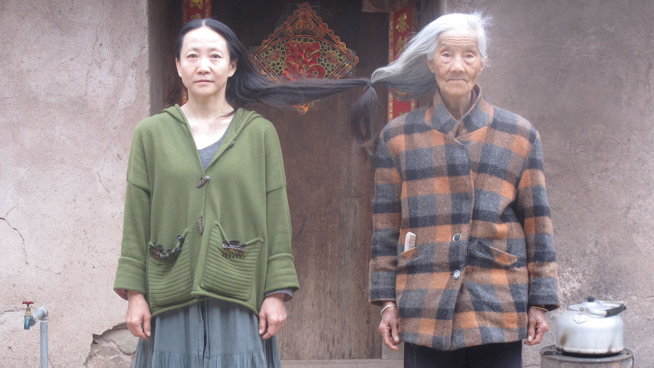 Two women standing next to each other, their long hair tied in a knot connecting them together.