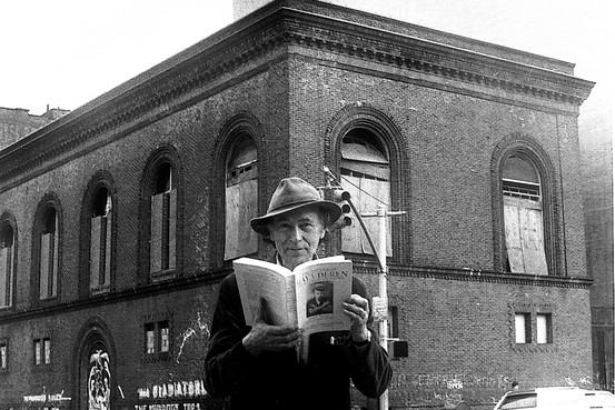 Man wearing a hat, holding a book open, in front of the building for Anthology Film Archives