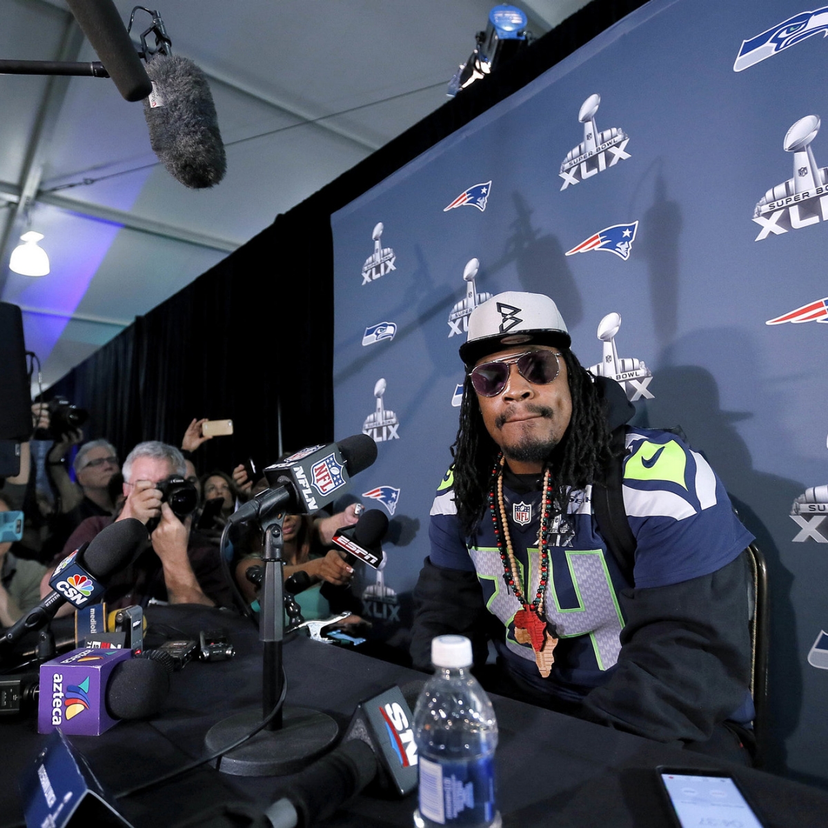 Marshawn Lynch sitting at a table surrounded by microphones