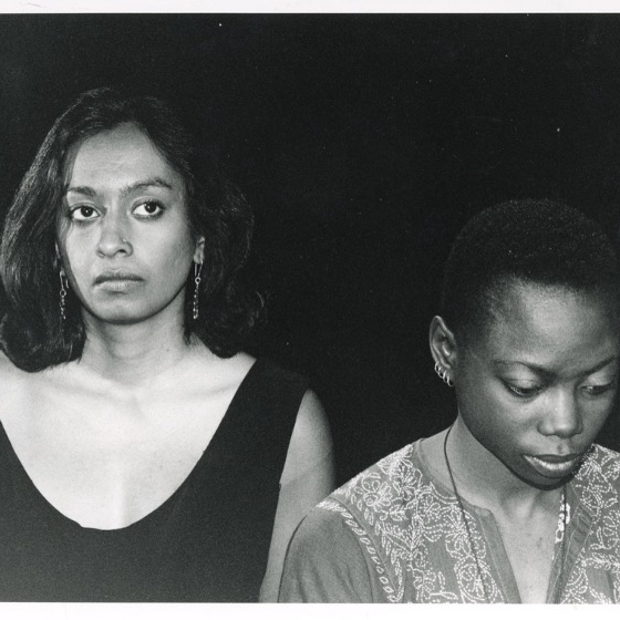 Two people stnading against a black background looking away from the camera