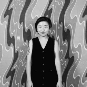 Medium shot of a woman with short hair wearing a dark dress standing in front of a decoarated wall.