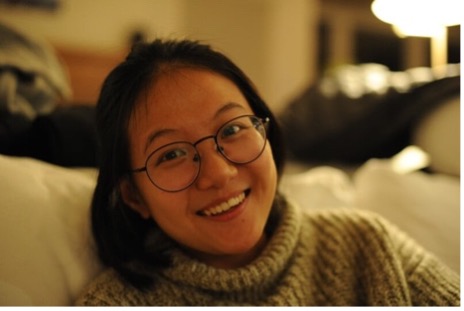 Woman with dark hair and circular glasses smiling.